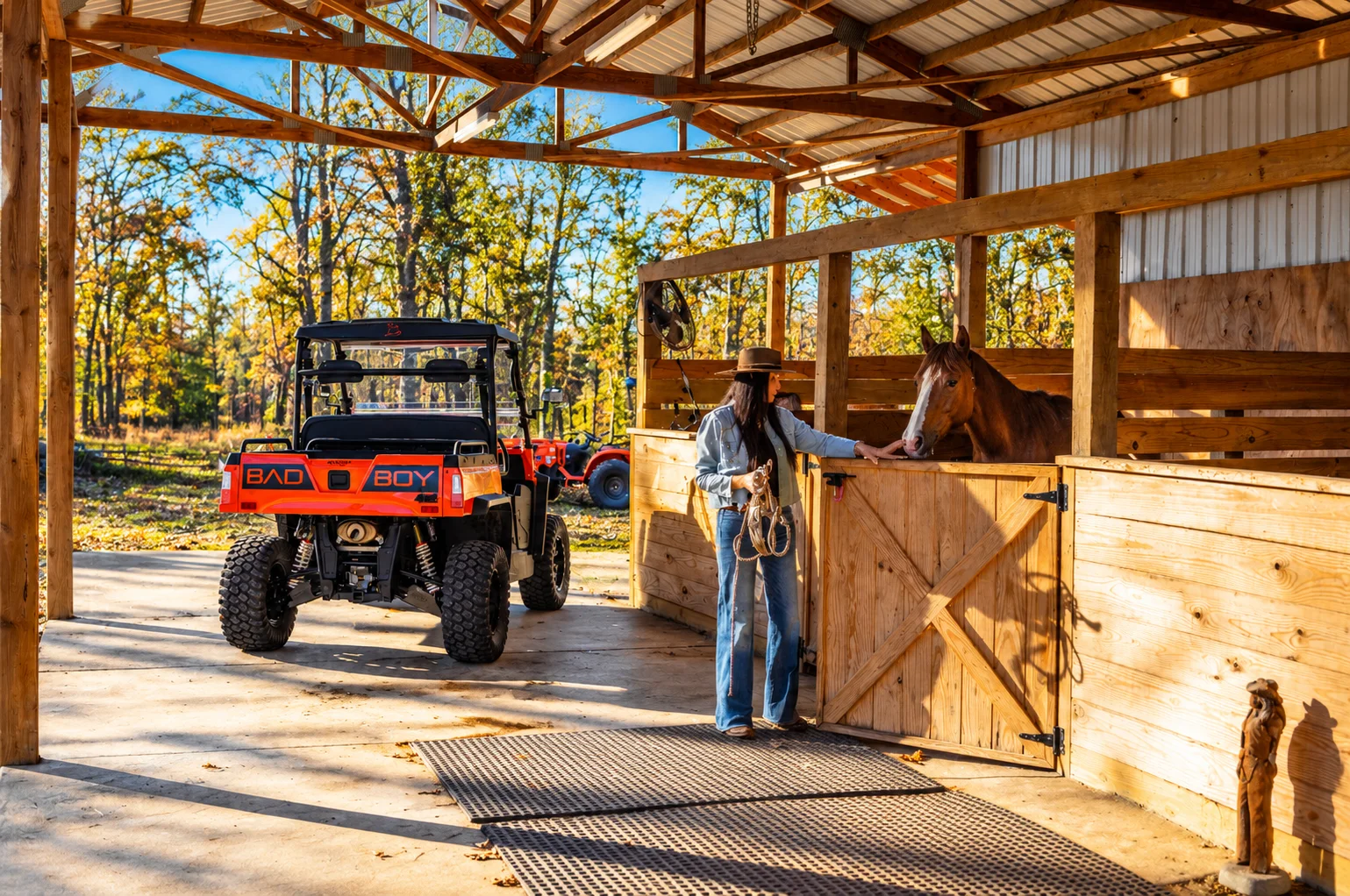 Cowgirl with a chestnut horse beside a Bad Boy utility vehicle in a barn
